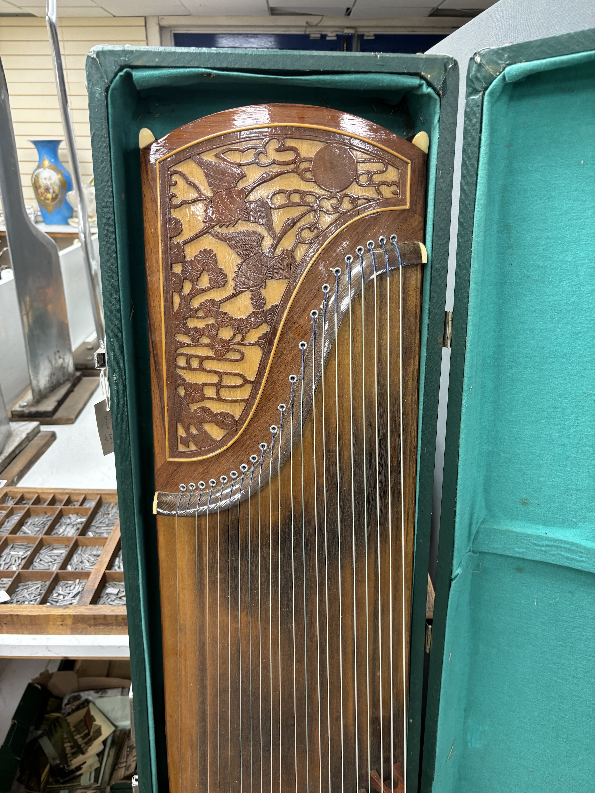 A cased Chinese Guzheng zither harp, hardwood body with blind fretwork decorative panel of birds and trees, with 21 strings, in fitted hard case, 163cm long